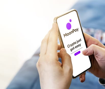 London, UK, March 2022: unrecognizable young female surfing on MoonPay website with a phone in her living room in the daytime. Crypto currency, Finance and business. Illustrative editorial.