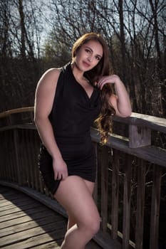 woman in black elegant dress standing on wood bridge in sunshine