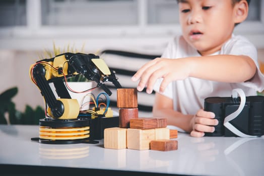 Happy Asian little boy using remote control playing robotic machine arm for pick up wood block, Funny learning successful getting a lesson control robot arm, Technology science education concept