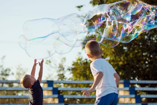 The little boys are playing with giant colorful soap bubbles outdoors, happy childhood and active life concept.