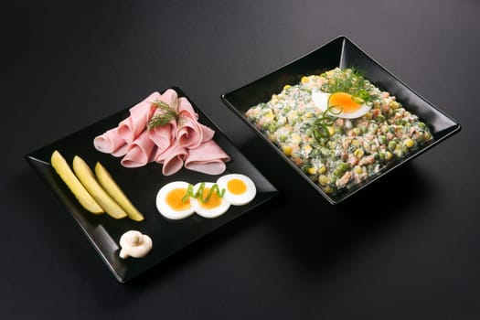 Gourmet appetizer from ham, eggs, pickle and french salad or russian salad served in black plates on black table in elegant restaurant.