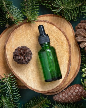 Green Pipette Dropper Bottle between fir branches and pine cones on wooden piece top view. Brand packaging mockup. Dark cream container for skincare product, cream or serum. Healthcare concept. Natural cosmetics.