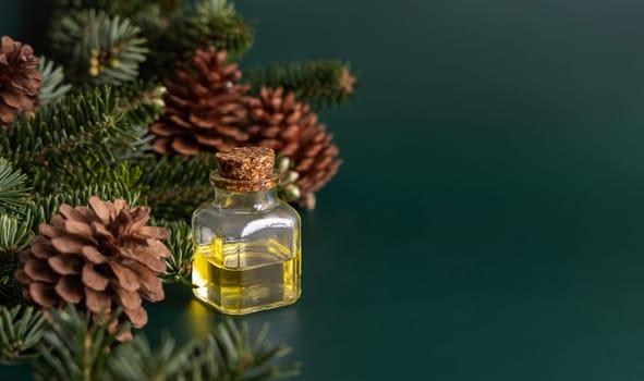 Glass bottle with conifer essential oil near fir branches and pine cones on green close up. Aromatherapy, spa and herbal medicine concept. Natural remedy or cosmetics.