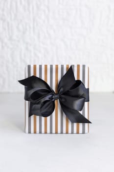 Gift box wrapped in Striped geometric paper with black ribbon bow close up. Christmas, New Year, Birthday, Anniversary concept