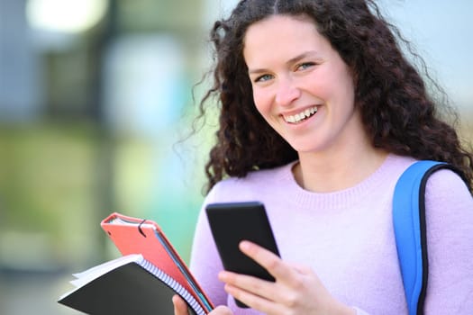 Happy student looking at camera holding phone