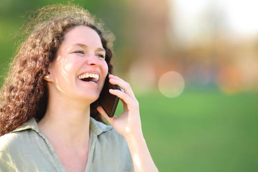 Happy woman laughing talking on phone in a park