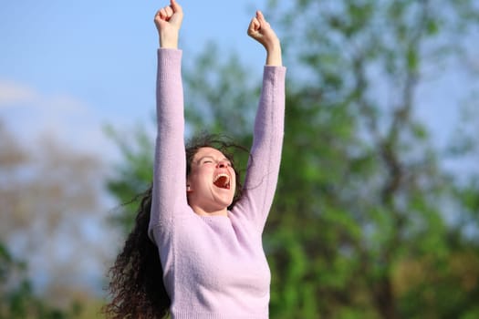 Excited woman raising arms in a park celebrating a good day