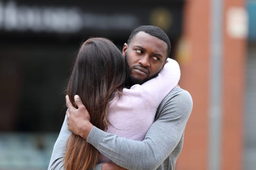 Disappointed man with black skin hugging a woman