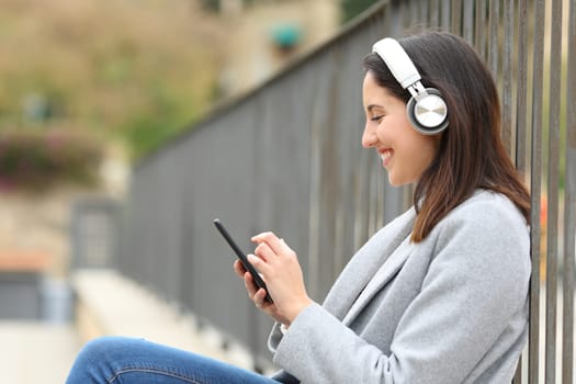 Happy woman listening to music on cell phone in the street