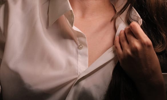 Beautiful girl with dark hair unbuttons the collar of a white shirt..