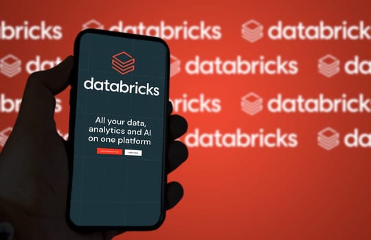 San Francisco, CA, US, May 2022: hand holding a phone with Databricks company web page on screen. In background the logo Databricks blurred and repeated. Databricks is an enterprise software company