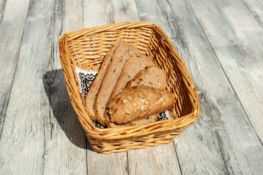 Closeup of slices of fresh baked whole grain bread in a wicker basket on a rustic bright wooden table. Health concept. Outdoor with natural sunlight.