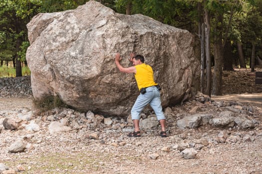 Man stands in front of a large rock. erratic boulder which was built by erosion.