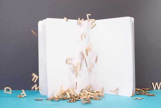 Open white book page, wooden letters falling down, school and education concept, copy space for text
