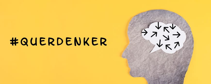 Think different stands in german language on the yellow background, head with brain, being a nonconformist, standing out from the crowd, conspirancy theory