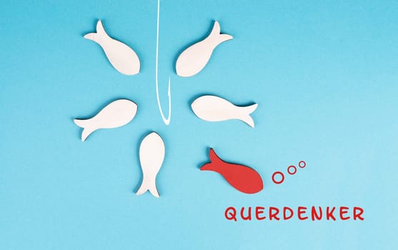 Think different stands in german language on the blue background, red fish is standing out from the crowd, being a nonconformist, conspiracy theory, group swims to the fishing rod