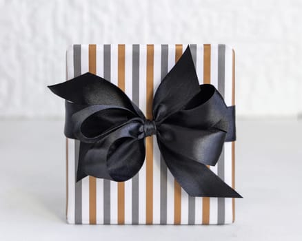 Gift box wrapped in Striped geometric paper with black ribbon bow close up. Christmas, New Year, Birthday, Anniversary concept