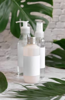 Trasparent cosmetic dispensers and tropical monstera leaves on marble table close up. Brand packaging mockup. Skincare beauty products. Natural homemade cosmetic bottles..