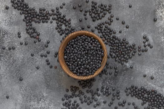 Wooden bowl of black beluga lentils beans on grey table top view. Healthy eating, protein source for vegan and vegetarian diet. Traditional Asian and North African cuisines ingredient