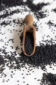 Wooden scoop of Indian spice Black cumin (nigella sativa or kalonji) seeds close up on white table. Traditional asian medicine, healthy eating, vegetarian and vegan food concept