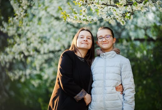 Mom with teenage daughter on the background of flowering spring trees. Woman and girl in the park. Selective focus.
