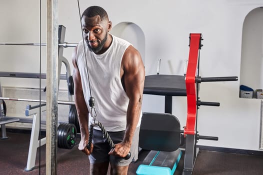 An African-American man is engaged in the gym on simulators. A pumped-up athlete goes in for sports on heavy weight simulators.