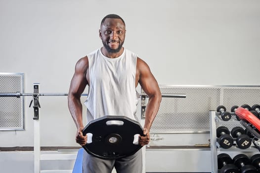 An African-American man in the gym holds a metal pancake in his hands. High quality photo