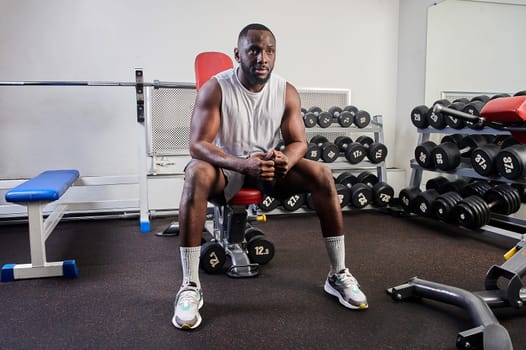 An African-American man is sitting on a bench bench in the gym and resting. High quality photo