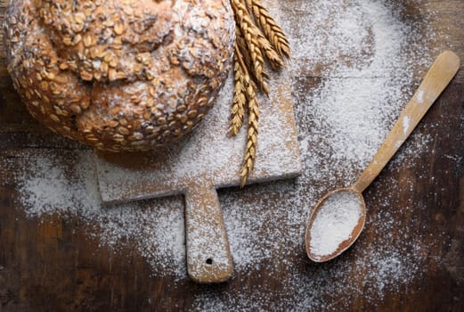 Homemade bread, flour, wheat ears and kitchen utensils on rustic table.