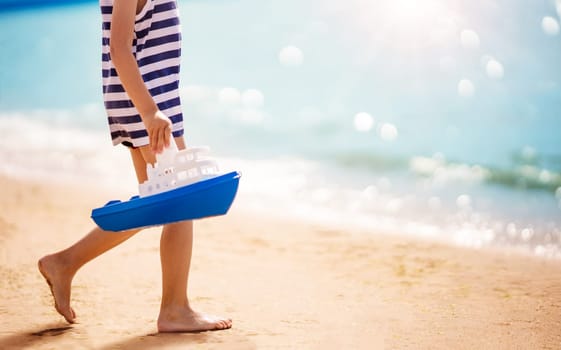 Little boy playing on the sea beach with toy ship. Concept of childhood and family vacation.