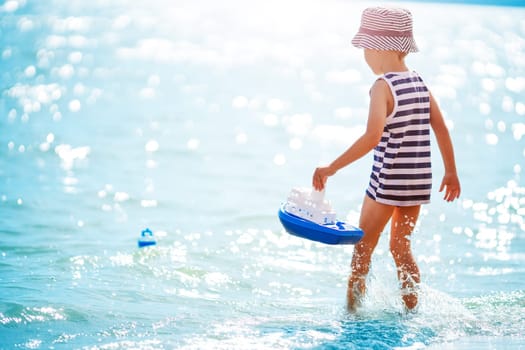Little boy playing on the sea beach with toy ship. Concept of childhood and family vacation.