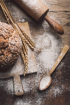 Homemade bread, flour, wheat ears and kitchen utensils on rustic table.