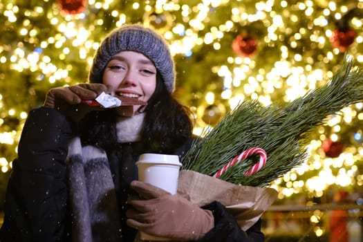 young beautiful happy Face of smiling girl posing. Christmas tree on background. Happy New Year eating Chocolate with coffee cup and candy