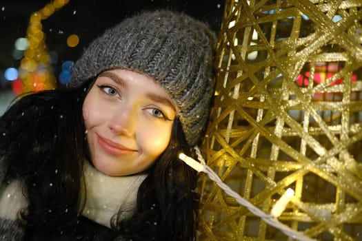 Outdoor of young beautiful happy smiling girl posing in street. Festive Christmas fair on background. Model wearing stylish clothes. Happy New Year Face with yellow lights near