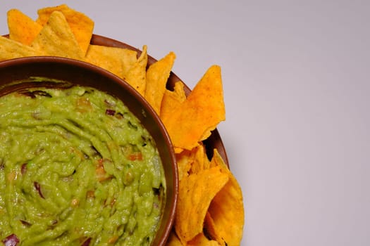 Mexican guacamole sauce and tortilla chips on a isolated white background. Guacamole bowl with nachos chips. Place for text, close up view of a part the plate.