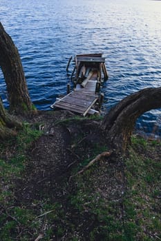 Autumn scene - lake and destroyed wooden pier. Old rotten wooden pier with missing planks with bench on a lake in the forest at autumn.