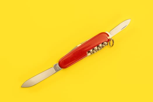 Tabletop view, red pocket knife, with both blades opened, laying on yellow board.