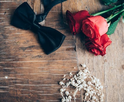 Bow tie, peals and roses on rustic wooden table. Wedding concept. Retro filter.