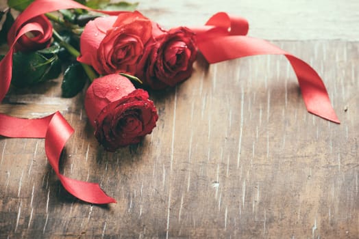 Red valentine roses decorated with red ribbon on rustic wooden table. Retro filter.