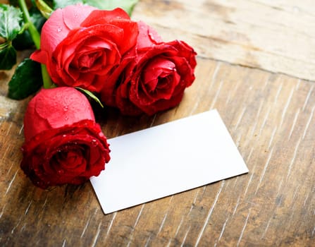 Red roses with empty card on wooden table. Valentine concept.