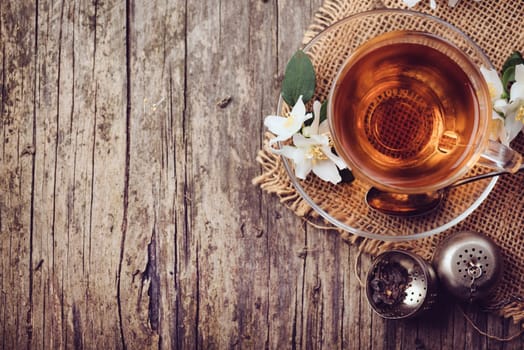 Cup of tea and jasmine flower on rustic wooden table, Top view.
