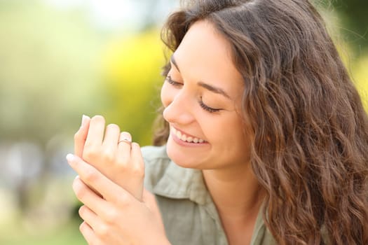Happy woman looking at wedding ring after engagement in a park