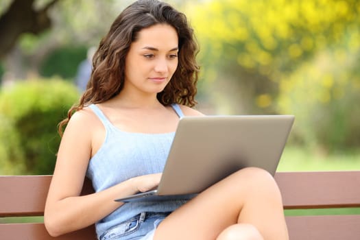 Happy woman using laptop sitting on a bench in a beautiful park