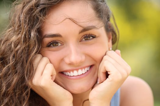 Front view portrait of a beautiful woman with perfect white smile looking at camera in a park