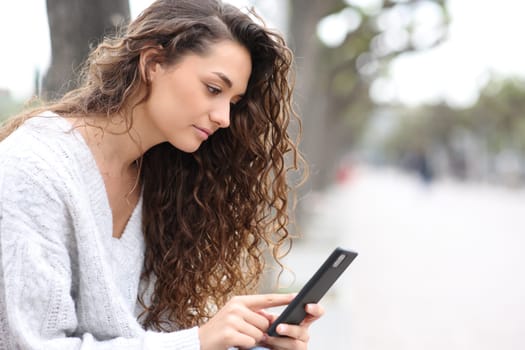 Serious woman using cell phone sitting on a bench in the street