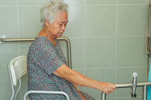 Asian elderly old woman patient use toilet support rail in bathroom, handrail safety grab bar, security in nursing hospital.