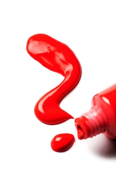 Close-up of an open tube of artist paint with red acrylic paint spilling out in the shape of a question mark on a white background.