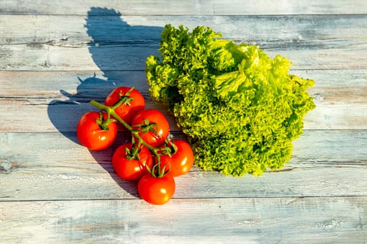 Closeup of healthy fresh tomatoes and green salad on a rustic bright wooden table. Health concept. Outdoor with natural sunlight.