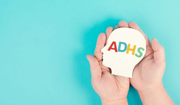 Hands holding a head with the german word ADHS which means attention deficit hyperactivity disorder, ADHD symptom, mental health