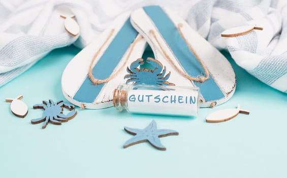 Blue colored summer and vacation background, flip flops, sea stars and a glass bootle with the word coupon in german language, holiday, travel and tourism concept